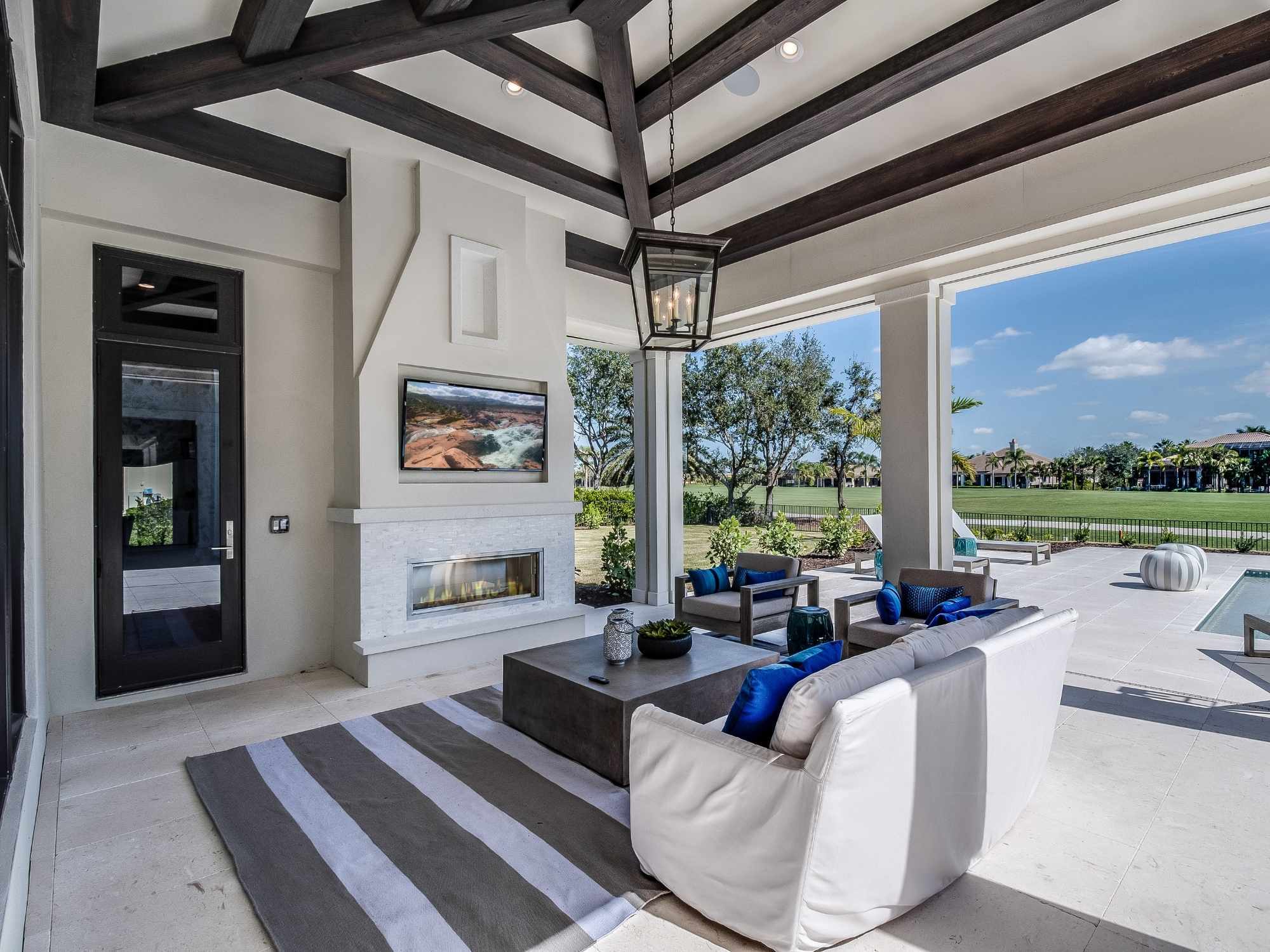 Luxury outdoor patio with vaulted ceilings, dark wood beams, a stone fireplace, comfortable seating - optimized